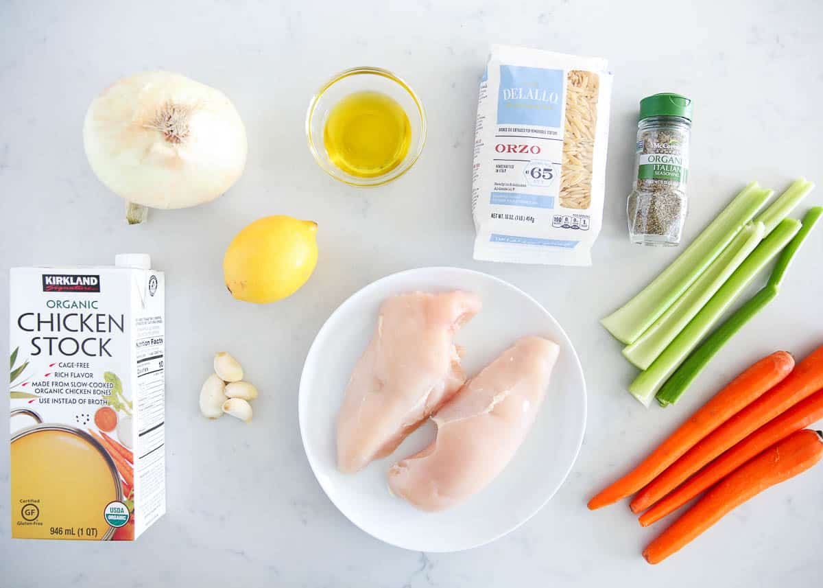 Chicken and orzo soup ingredients on marble counter.