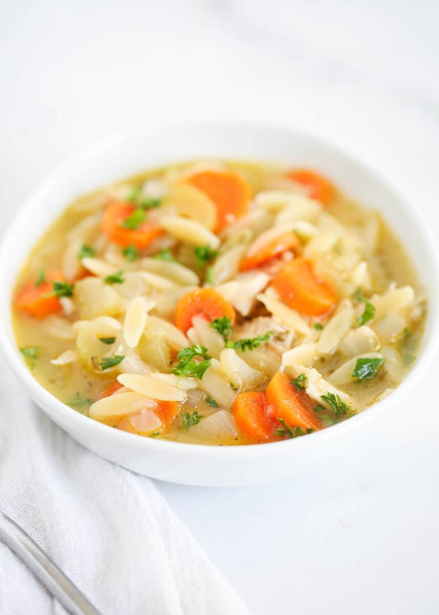 Chicken orzo soup in a white bowl.