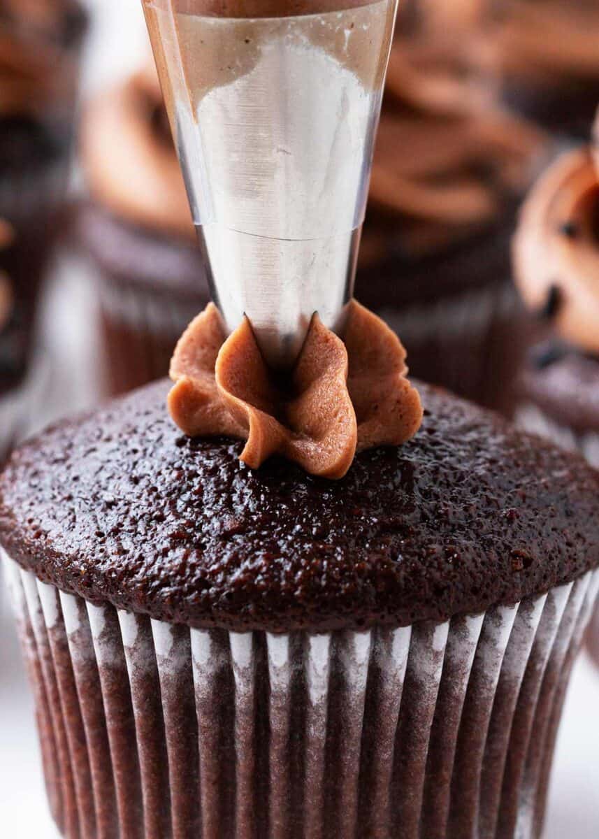 Piping chocolate frosting onto chocolate cupcake.