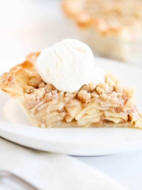 Slice of dutch apple pie on a white plate with ice cream.