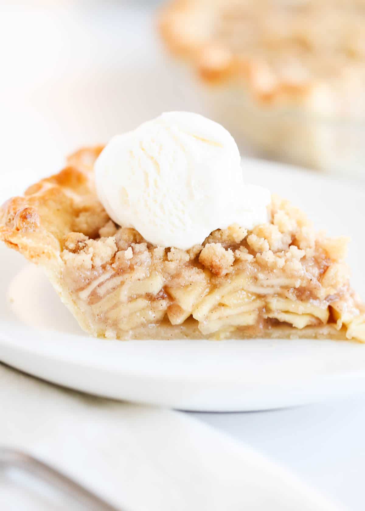 Slice of dutch apple pie on a white plate with ice cream.