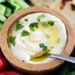 Homemade hummus in a wooden bowl with vegetables.