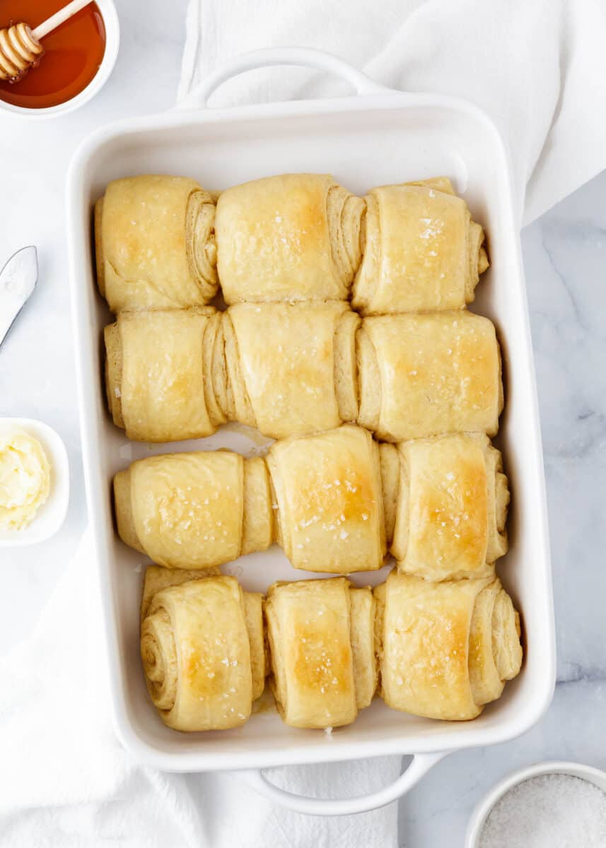 Baked parker house rolls in a white baking dish with honey.
