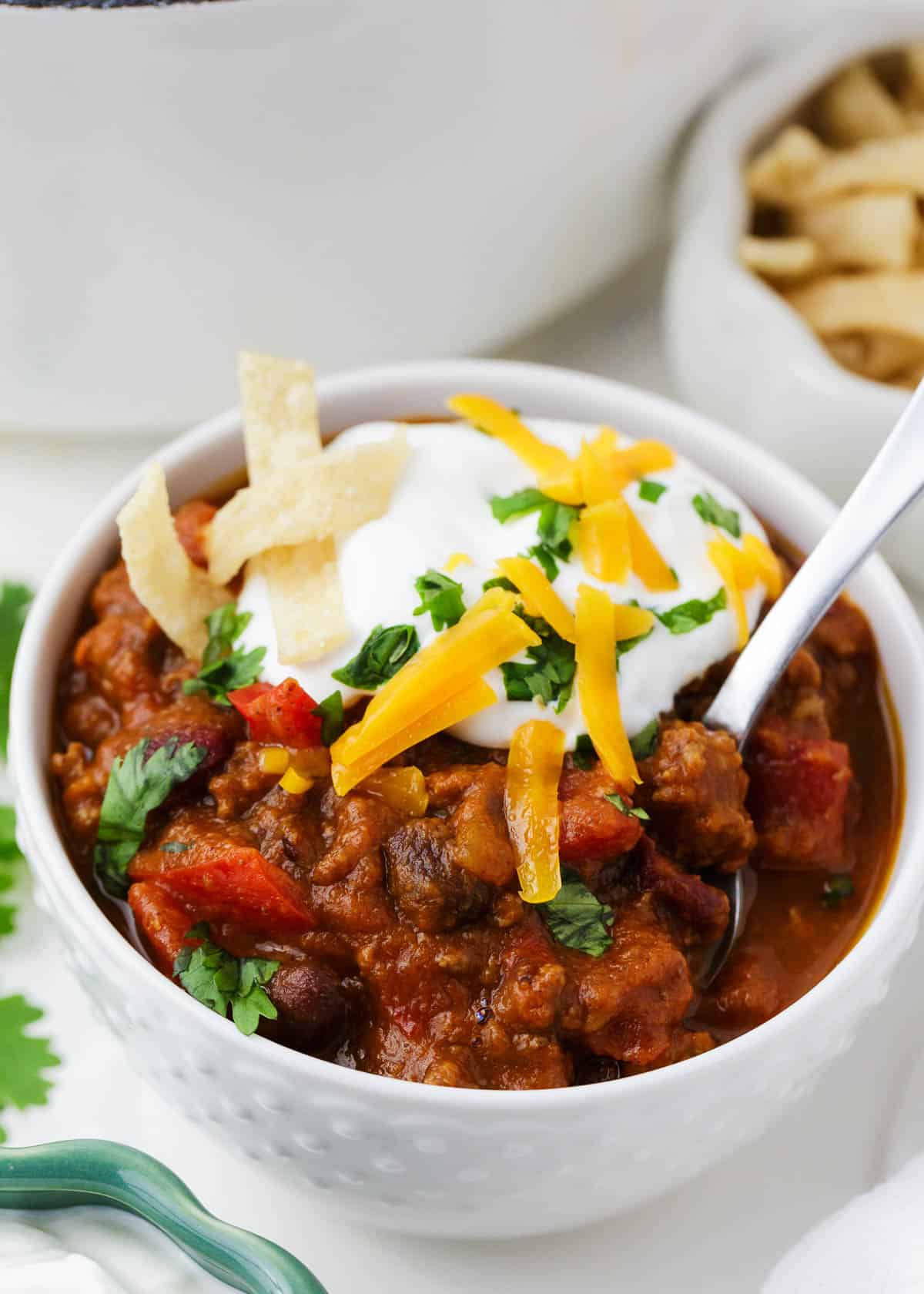 This easy pumpkin chili is comforting, filling and full of fall flavors. A savory pumpkin dish that you'll want to enjoy all season long! Pumpkin chili in a white serving bowl with sour cream, cilantro and shredded cheese garnish.