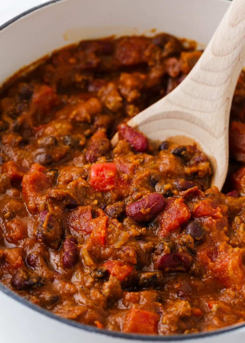 Pumpkin chili in a white pot with a wooden spoon.