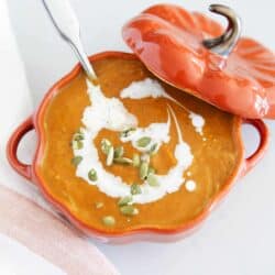 Pumpkin soup in a pumpkin bowl with pumpkin seeds on top.