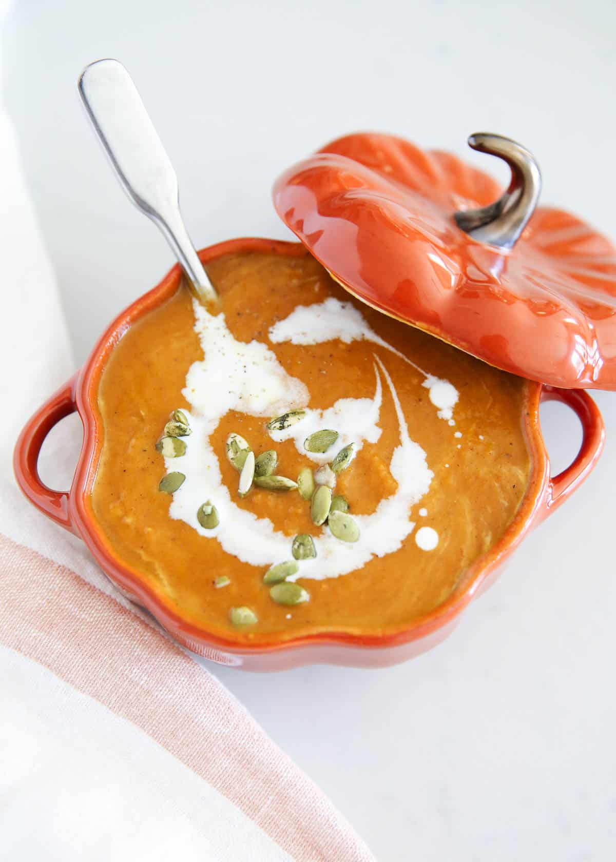 Pumpkin soup in a pumpkin bowl with pumpkin seeds on top.