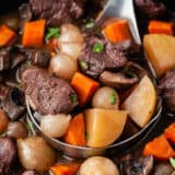 Ladle full of beef bourguignon in a slow cooker.