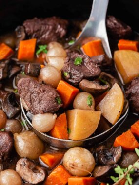 Ladle full of beef bourguignon in a slow cooker.