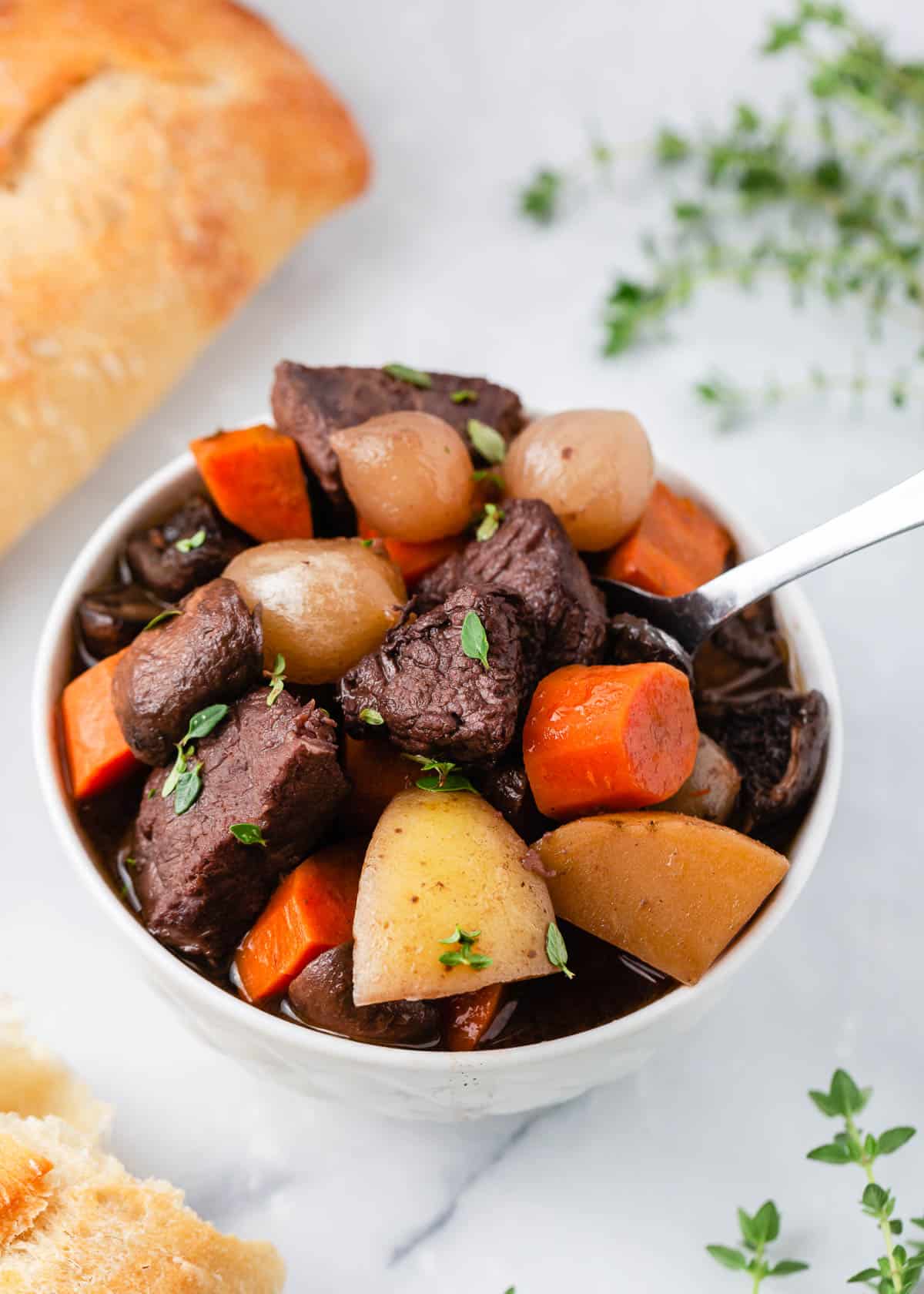 Beef bourguignon in a white bowl with bread.