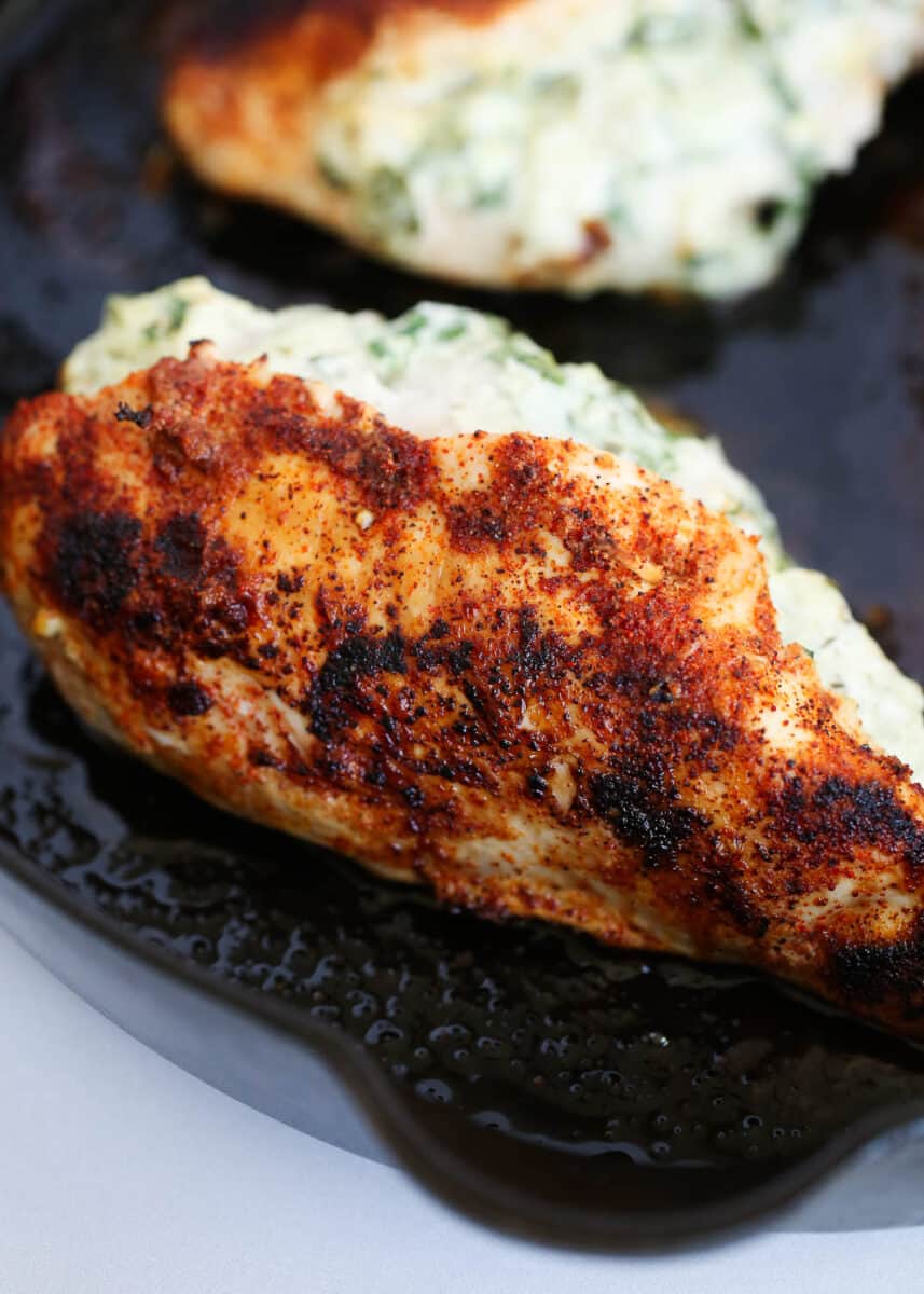 Spinach stuffed chicken breast cooking in an iron skillet.