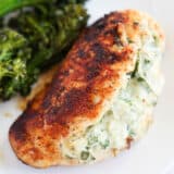 Spinach stuffed chicken breast cooking on a white plate with broccoli.