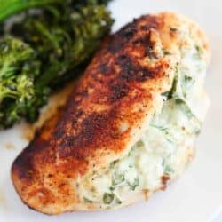 Spinach stuffed chicken breast cooking on a white plate with broccoli.