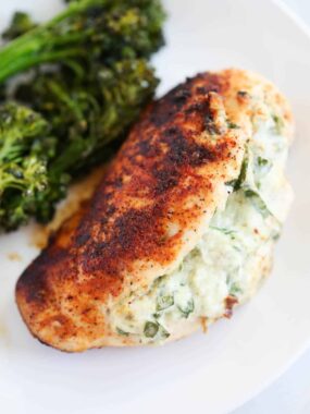Spinach stuffed chicken breast cooking on a white plate with broccoli.
