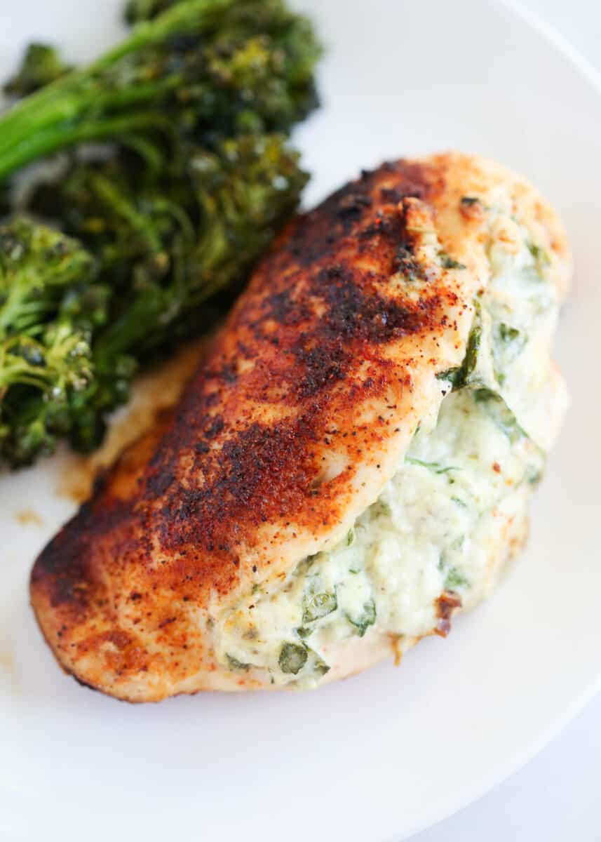 Spinach stuffed chicken breast cooking on a white plate with broccoli.