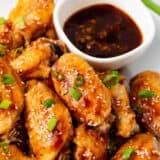 Teriyaki chicken wings on white plate with teriyaki sauce.