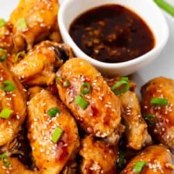 Teriyaki chicken wings on white plate with teriyaki sauce.