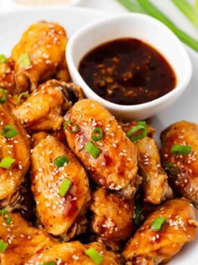 Teriyaki chicken wings on white plate with teriyaki sauce.