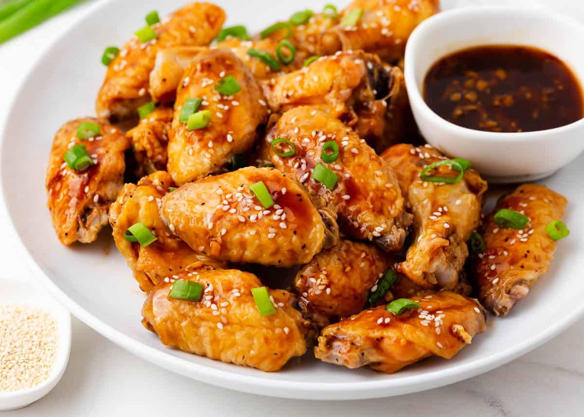 Oven-baked teriyaki chicken wings are healthier than frying but just as crispy. After baking, they're tossed in a homemade teriyaki sauce which adds the best flavor! Oven baked teriyaki chicken wings on a white plate with teriyaki sauce.