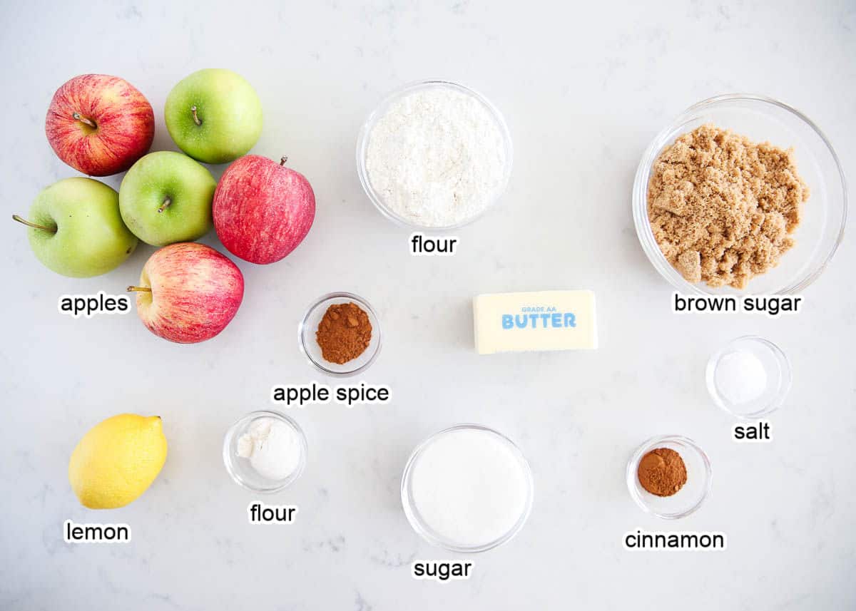 Apples, brown sugar, flour, apple spice, butter, cinnamon, lemon, sugar and salt on counter.