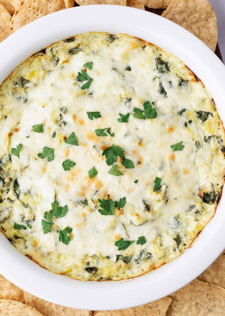 Spinach artichoke dip in a white pie dish with chips.