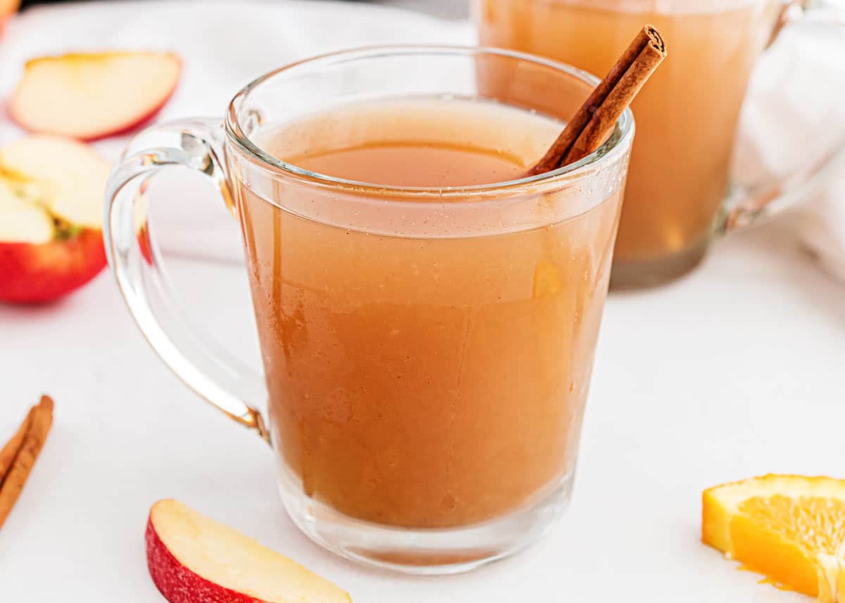 Cup of apple cider with cinnamon stick sitting on counter. 