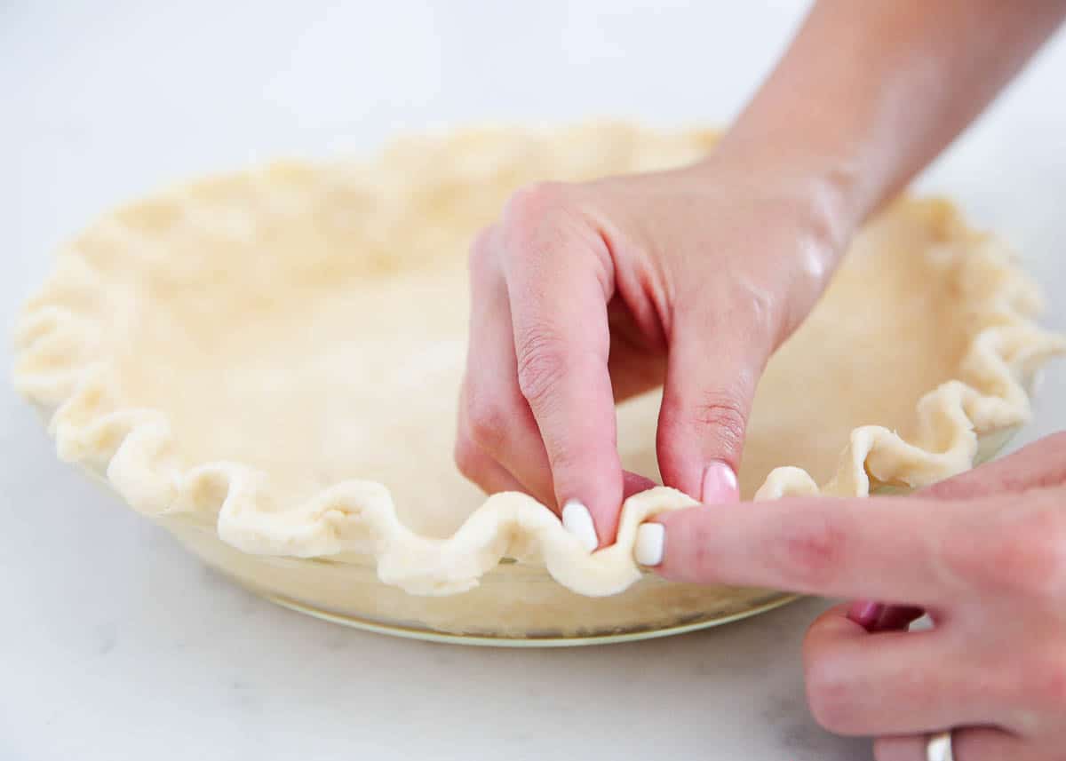 Fluting the edge of a pie crust with hands.