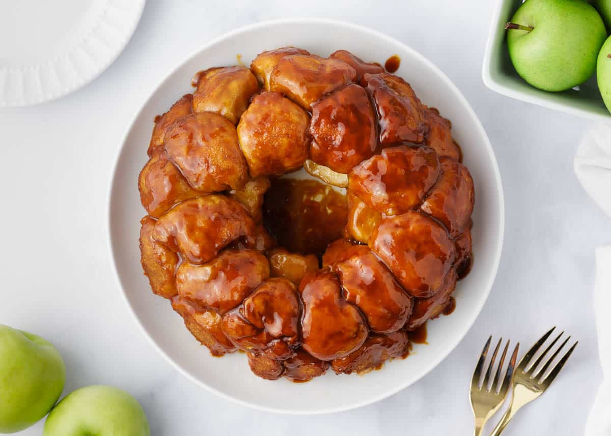 Ooey gooey sticky bread filled with cinnamon sugared apples. This caramel apple monkey bread is perfect for entertaining and makes the best fall treat! Caramel apple monkey bread on a white plate.