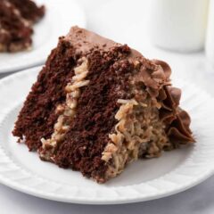 Slice of German chocolate cake with coconut pecan frosting and chocolate buttercream on a white plate.