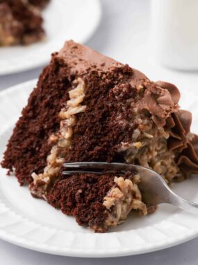 Slice of German chocolate cake with coconut pecan frosting being cut with a fork.