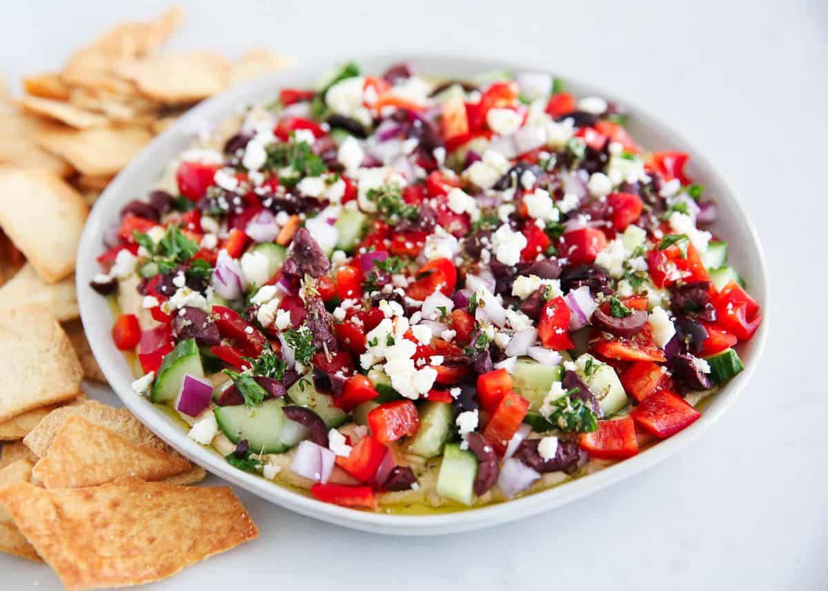 Layered Greek dip on a plate with pita chips.