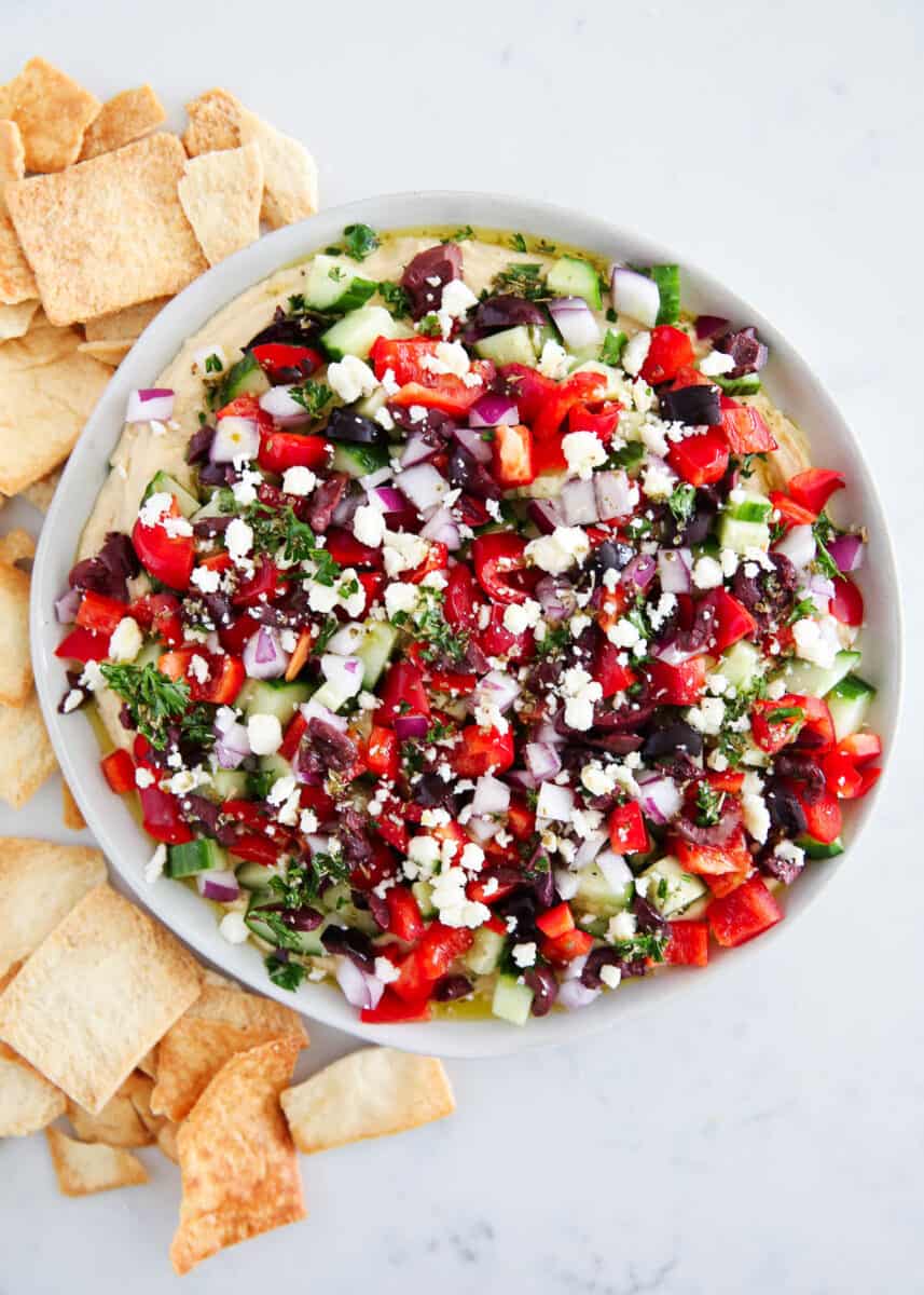 Layered Greek dip with feat on a plate with pita chips.