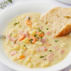 Ham and potato soup in a white bowl with bread.