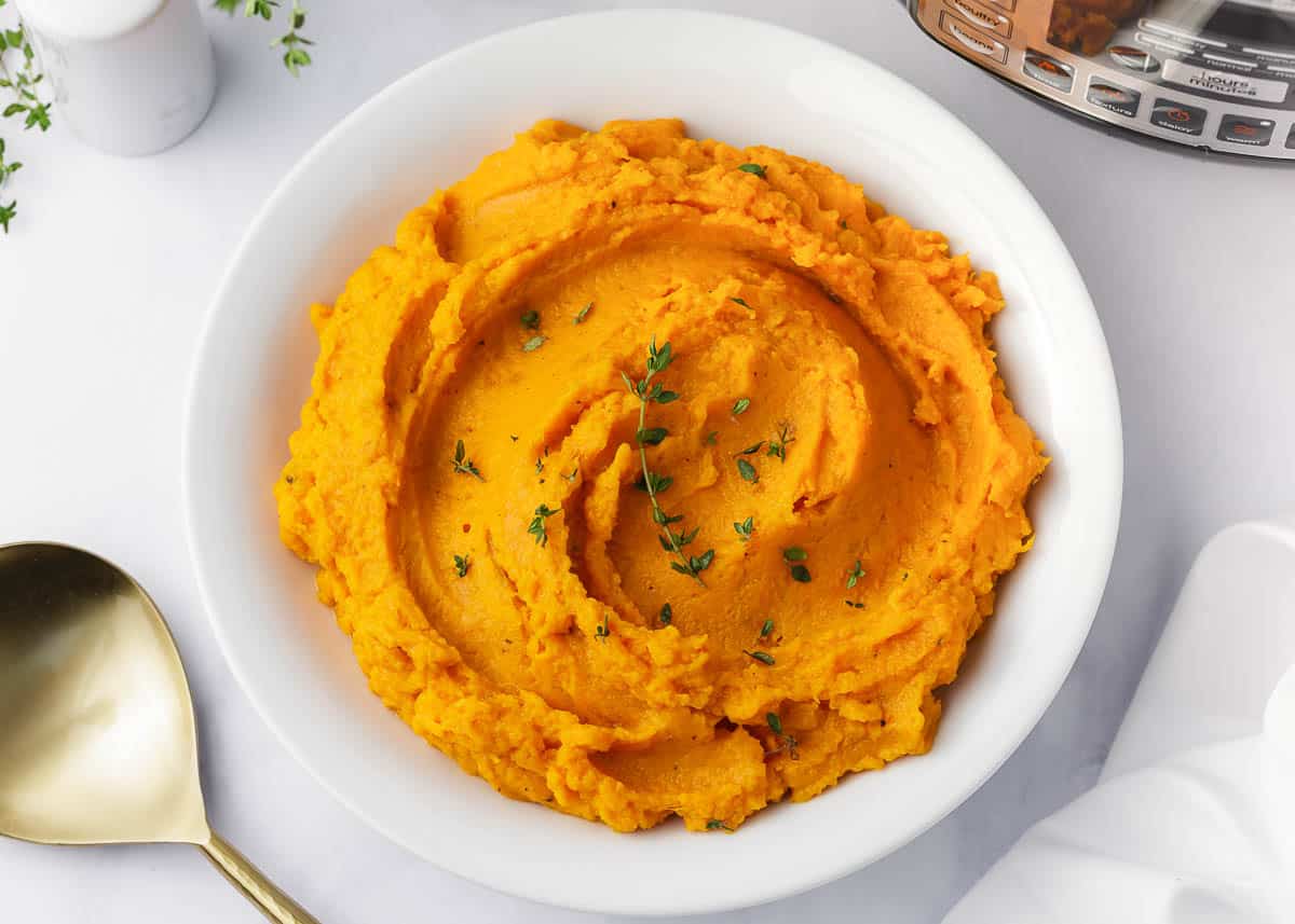Mashed sweet potatoes in a white bowl on counter. 