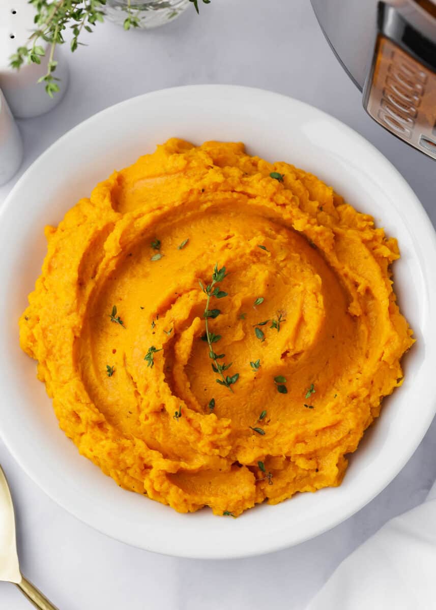 Mashed sweet potatoes with thyme in a white bowl.