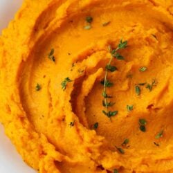 Mashed sweet potatoes and thyme in a white bowl.