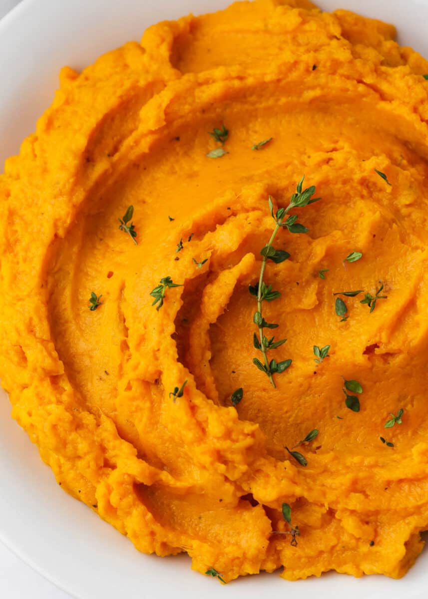 Mashed sweet potatoes and thyme in a white bowl.