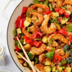 Cooked Kung pao shrimp in a white pot with chopsticks.