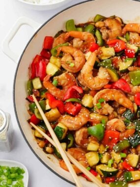 Cooked Kung pao shrimp in a white pot with chopsticks.