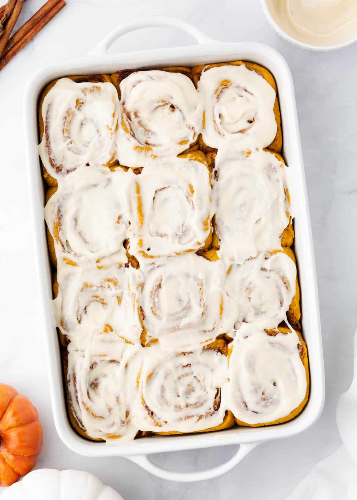 Pumpkin cinnamon rolls in a white baking dish.