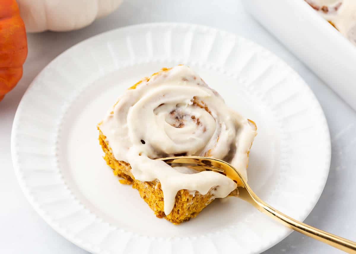 A pumpkin cinnamon roll on a white plate with a fork.