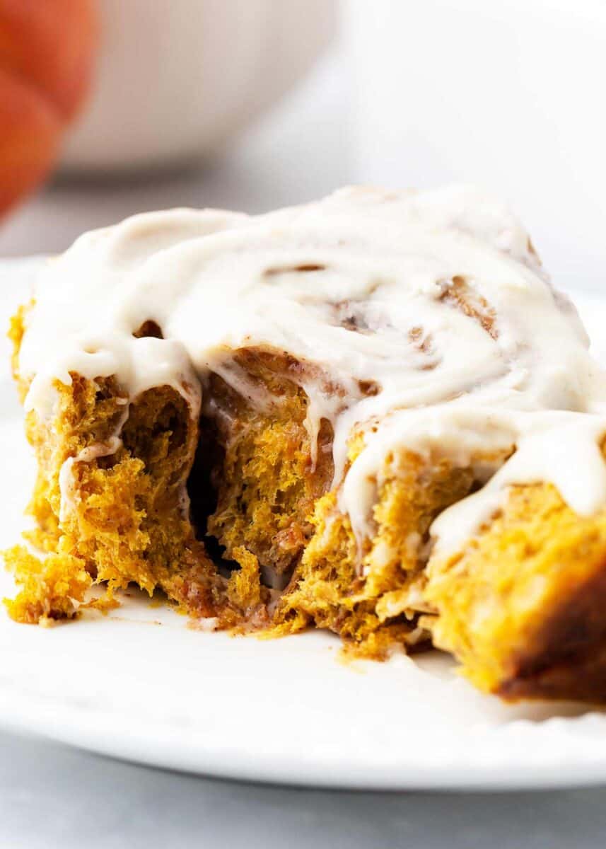 A bite taken from a pumpkin cinnamon roll on a white plate.