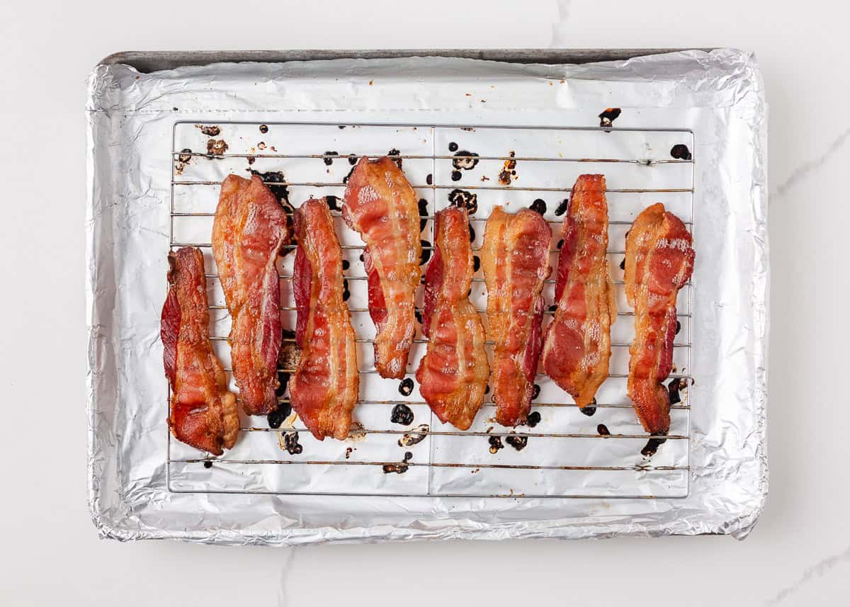 Overhead view of oven-baked bacon strips on a wire rack set over a foil-lined baking sheet, cooked until crispy and golden brown.
