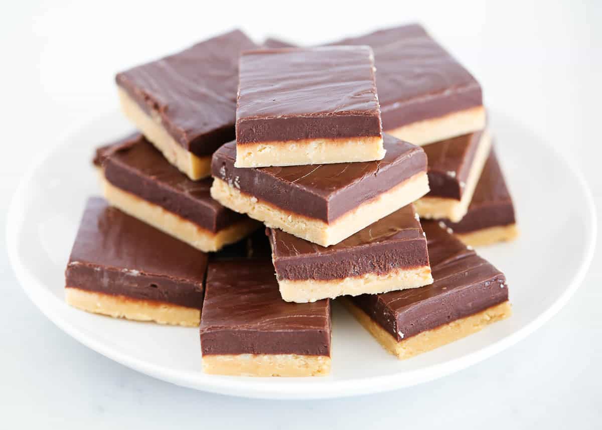 This 4-ingredient chocolate peanut butter fudge is made in just minutes using a microwave and a bowl! This chewy, decadent, sweet fudgy goodness is perfect for satisfying your sweet cravings and pretty enough for any holiday dessert table! Chocolate peanut butter fudge on the white plate.