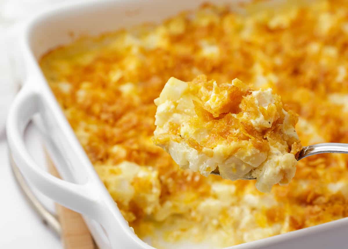 Spoonful of funeral potatoes in a white baking dish.