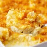Spoonful of funeral potatoes on a white baking dish.