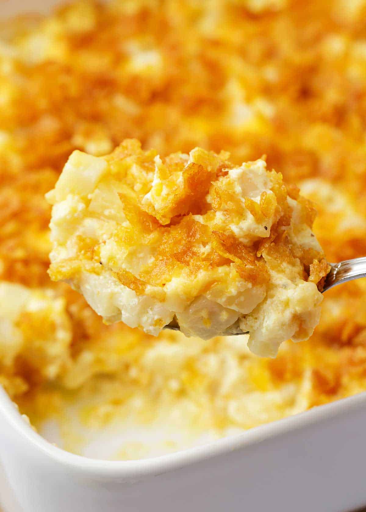 Spoonful of funeral potatoes on a white baking dish.
