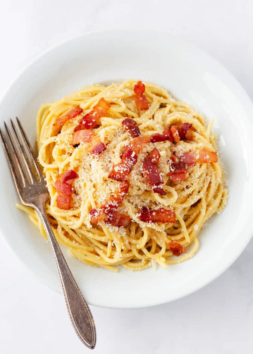 Pasta carbonara on a white plate with fork and cheese on top. 