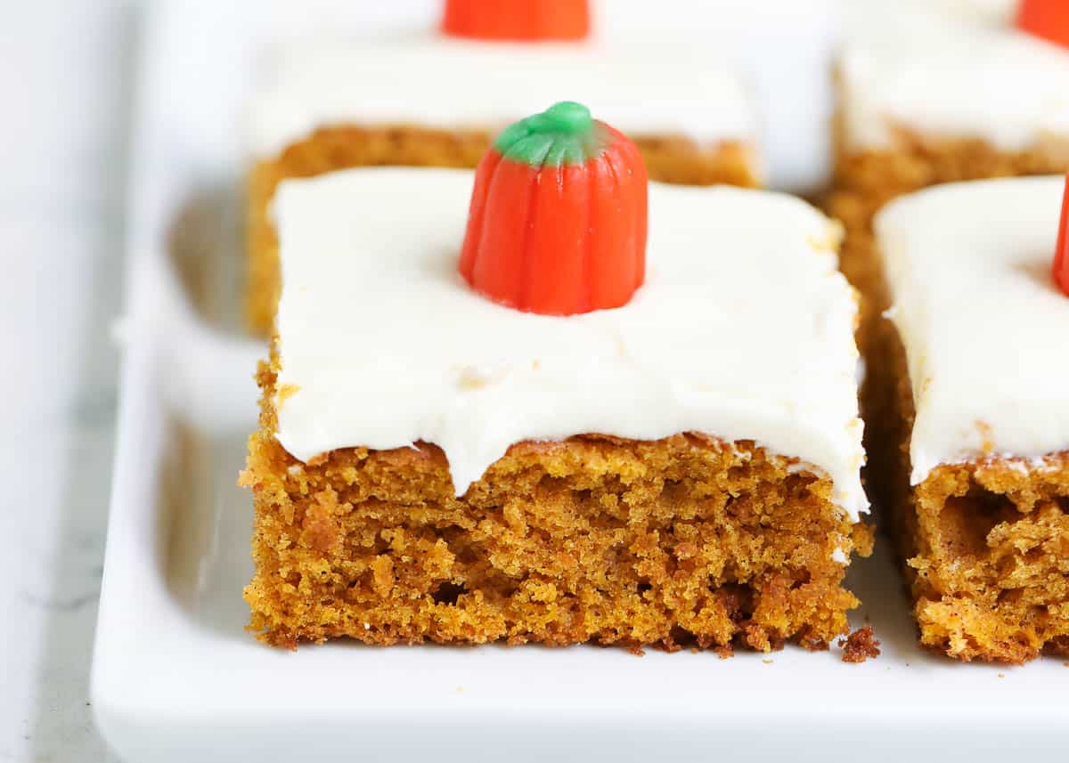 A super soft pumpkin spiced sheet cake topped with a delicious creamy topping. These are the absolute BEST pumpkin bars with cream cheese frosting! The best pumpkin bars on a plate.