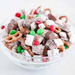 A close up of reindeer chow with powdered sugar cereal pieces, pretzels, peanut butter cups, and red and green M&M’s mixed together.